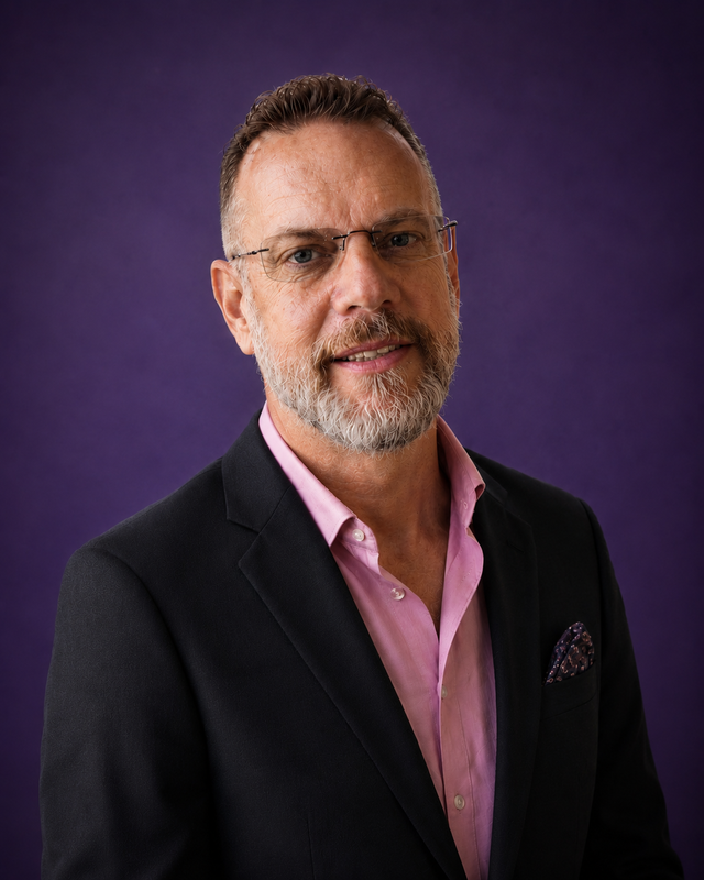 Chris Young, Cofounder, CEO and Principal Engineer at Embryonaut. Dark blazer, pink shirt, purple backdrop.